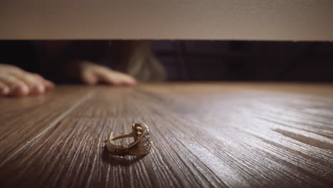 Woman-takes-out-lost-earring-under-couch-on-wooden-floor