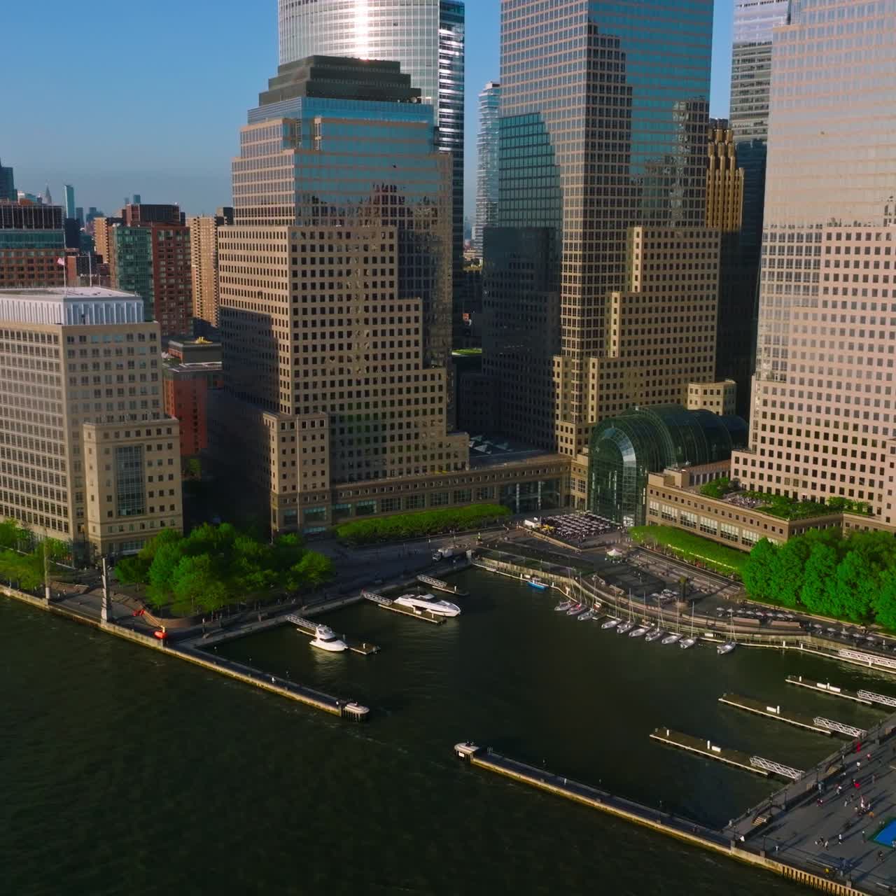 Huge skyscrapers towering over the river. Sun reflecting in the windows of the buildings. Little dock for yachts among the houses
