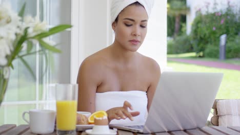 mujer joven usando una computadora portátil mientras desayuna