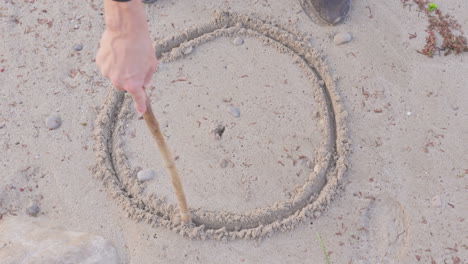 Un-Artista-Crea-Meticulosamente-Un-Círculo-Perfecto-En-La-Suave-Arena-Con-Un-Palo-De-Madera-Desgastado,-Demostrando-La-Belleza-Y-Precisión-Que-Se-Puede-Lograr-A-Través-De-Herramientas-Y-Técnicas-Simples.