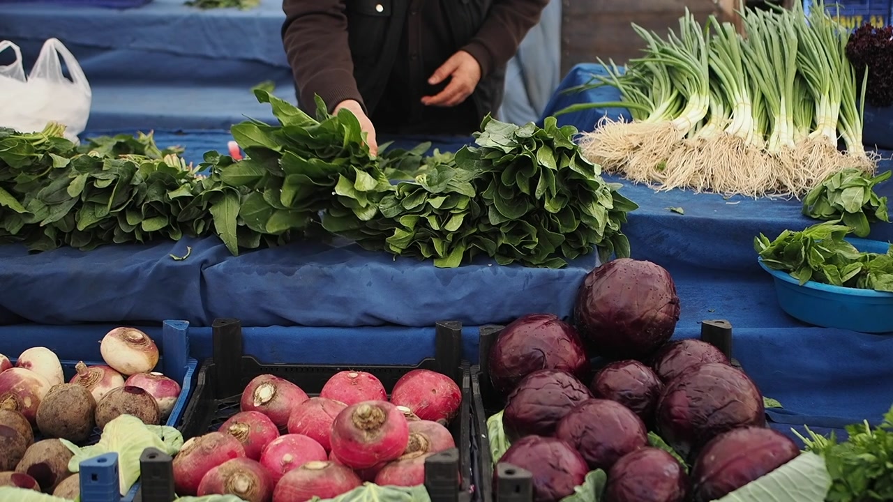 Person Arranging Fresh Spinach and Other Vegetables at a Market Stall