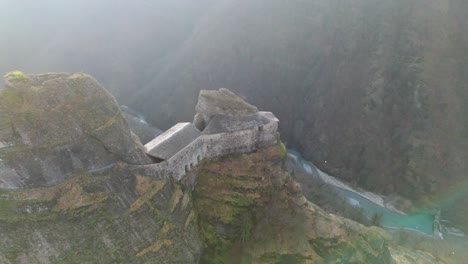 Majestuosa-Fortaleza-Antigua-En-Lo-Alto-De-Un-Acantilado-Escarpado-Con-Un-Río-Debajo-A-La-Luz-Brumosa-De-La-Mañana,-Vista-Aérea