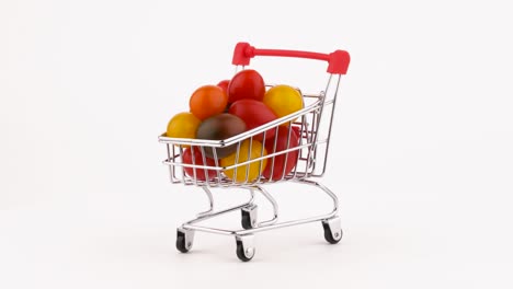 el carrito del supermercado está lleno de tomates cereza multicolores. rotando en la mesa giratoria. aislado en el fondo blanco. primer plano. macro.