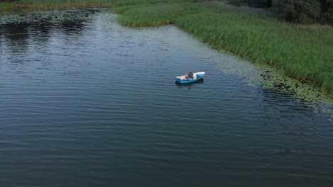 Aerial-zoom-out-shot-over-fisherman-on-floating-boat-in-lake