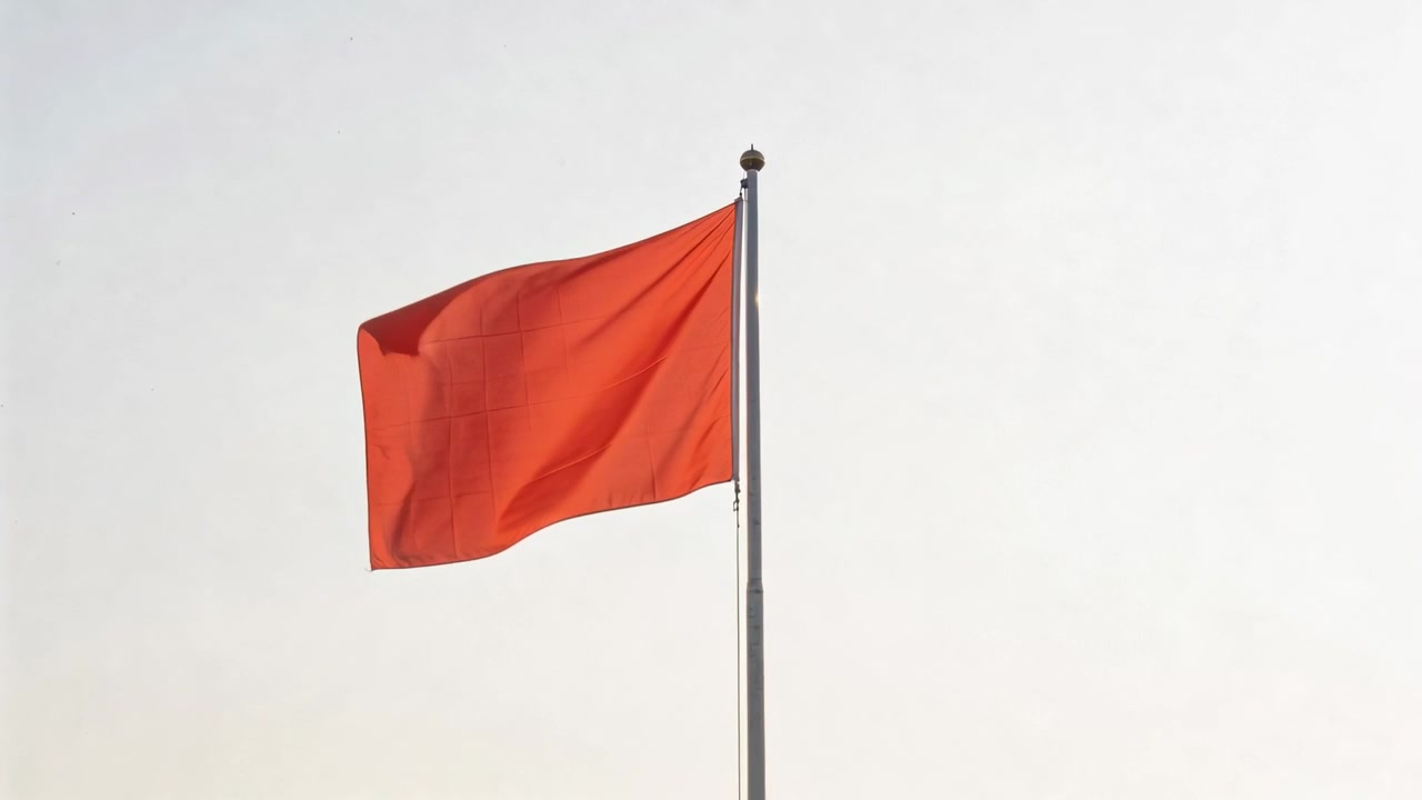 Bendera merah berkibar di tiang logam merespons hembusan angin di langit pucat, dengan tali bendera terlihat