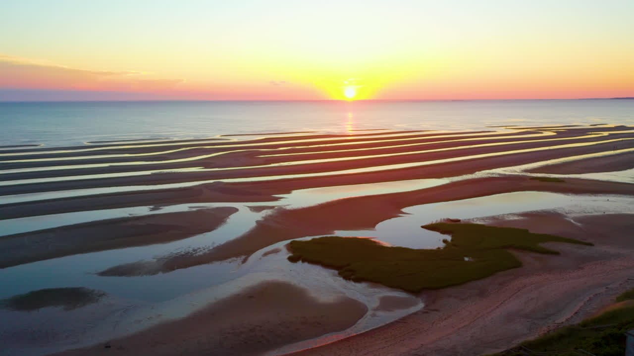 케이프 코드 베이 서사시 태양은 키 큰 푸른 잔디, 모래톱 및 웅덩이가 있는 썰물 때 여전히 해변의 공중 드론 영상을 설정합니다.