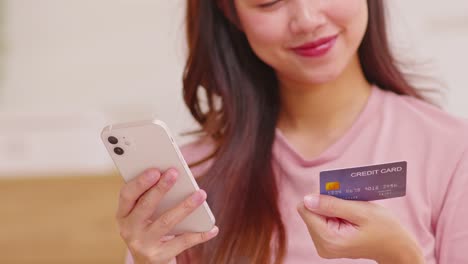 close up asian young woman using credit card for pay online shopping on mobile phone.hand typing credit card number to buying cloths from internet online store.digital payment technology concept