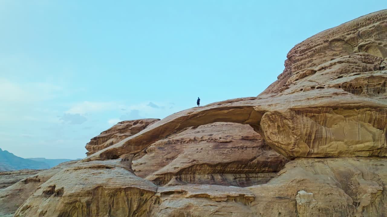 요르단 의 와디 럼 에 있는 부르다 바위 다리 의 자연 아치 위 에 서 있는 사람 의 공중 사진