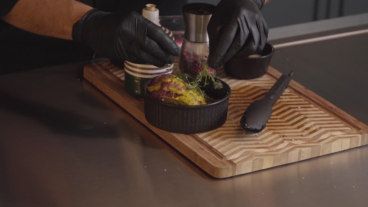 Gloved chef seasoning beef with mustard herbs and spices