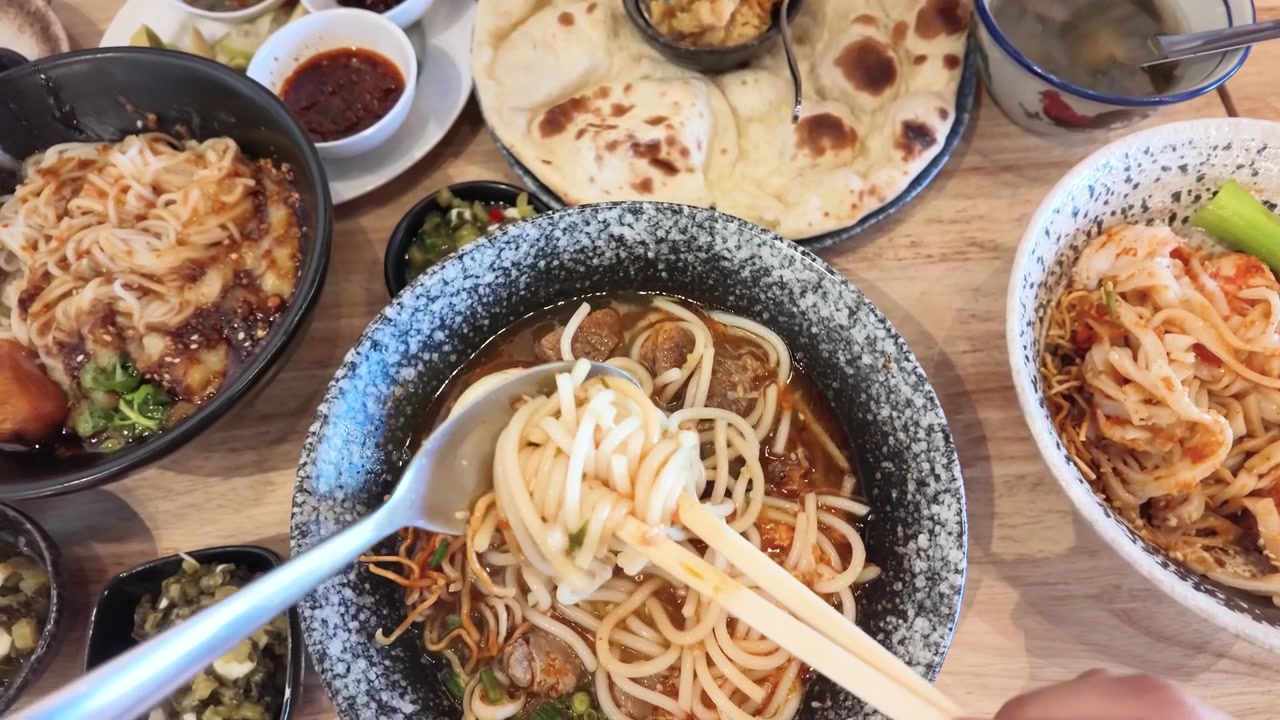 Pengambilan gambar dari atas: Tangan menggunakan sumpit dan sendok untuk makan mi Burma pedas di Bangkok.
