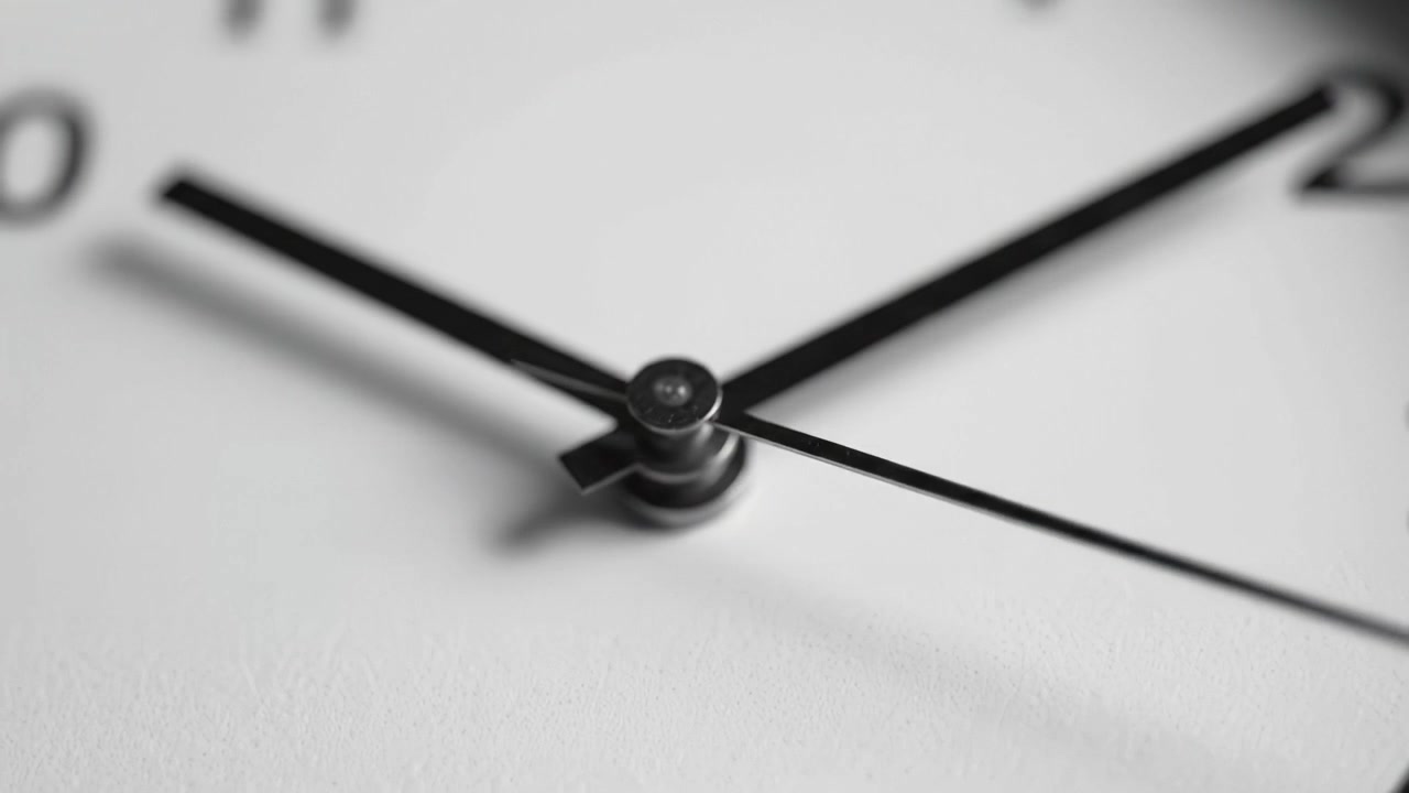Close-up of a clock's hands emphasizing the passage of time as they move, highlighting the detailed craftsmanship of a modern analog timepiece with a minimalist design.