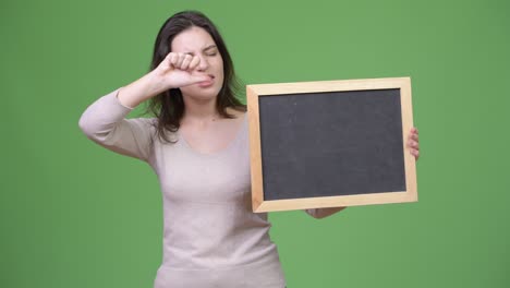 young beautiful woman giving thumbs down while holding blackboard