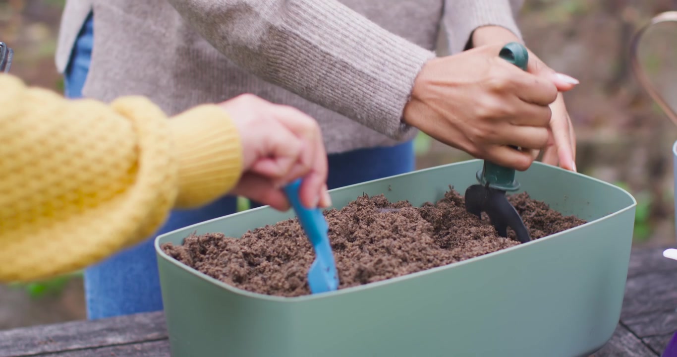 Donne afroamericane che smuovono il terriccio compattato in una fioriera verde con una paletta e una forchetta da giardinaggio, piantando semi.