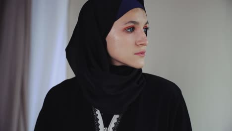 mujer musulmana pensativa en el vestido tradicional árabe abaya en fondo gris