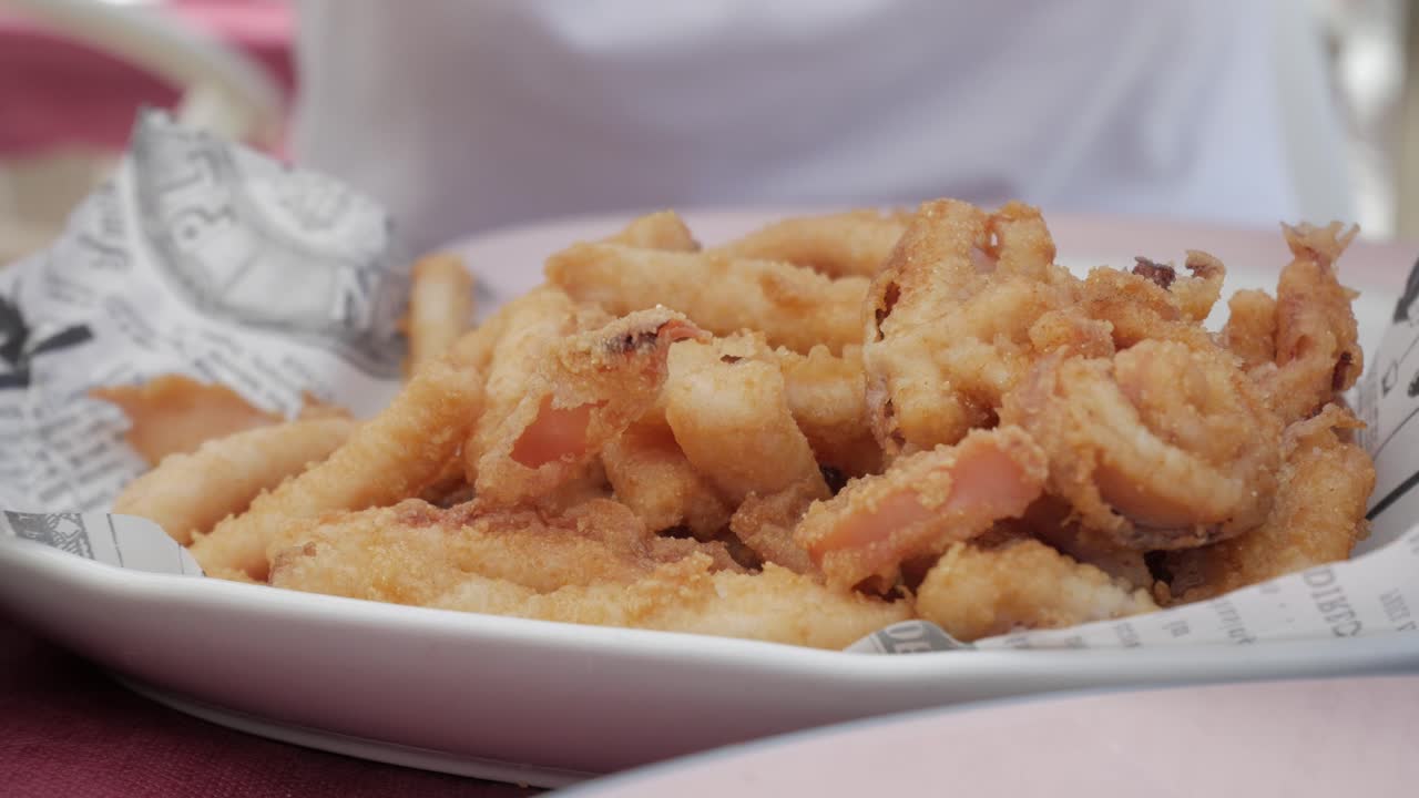 A plate of crispy fried squid tentacles being served, with a hand squeezing lemon
