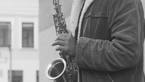 black and white and close up view of a man in jacket playing sax in the street