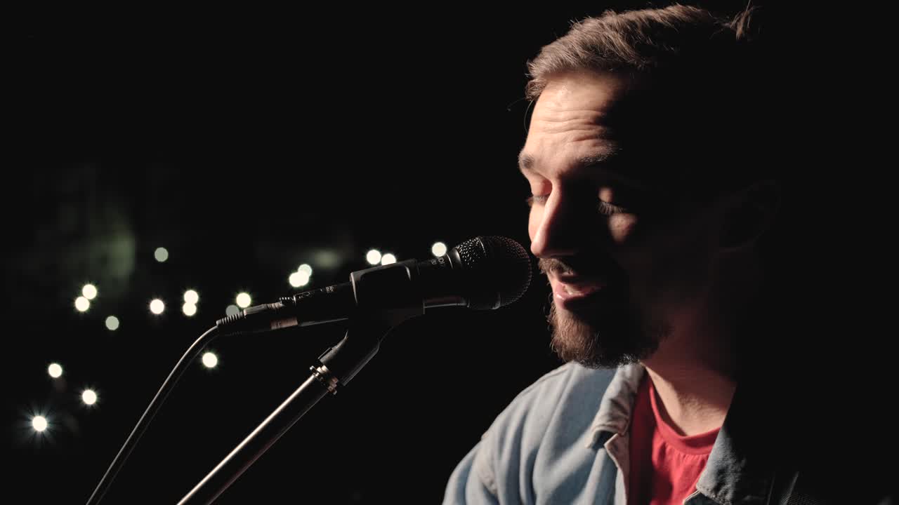 un músico está tocando la guitarra en un gran escenario con miembros de la audiencia sosteniendo linternas en el fondo. el auditorio está lleno de hermosas luces parpadeantes.
