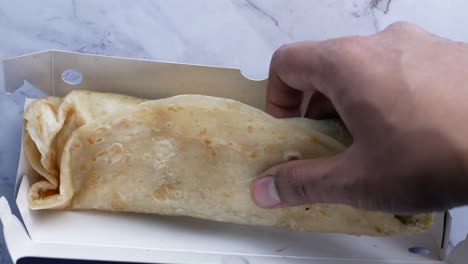 hand taking out a paratha wrap from a box