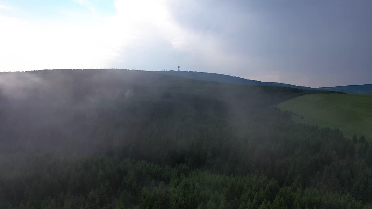 rolling clouds going past the drone, beautiful view over the sunny hills and the forest below