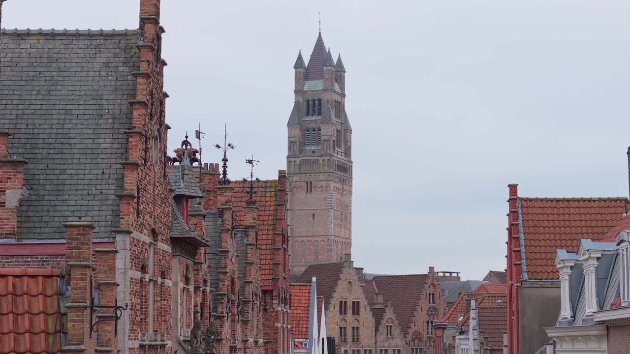 Un'inquadratura che cattura le pittoresche case di un quartiere di Bruges mentre il Belfry viene gradualmente rivelato, evidenziando il fascino medievale e lo skyline iconico della città