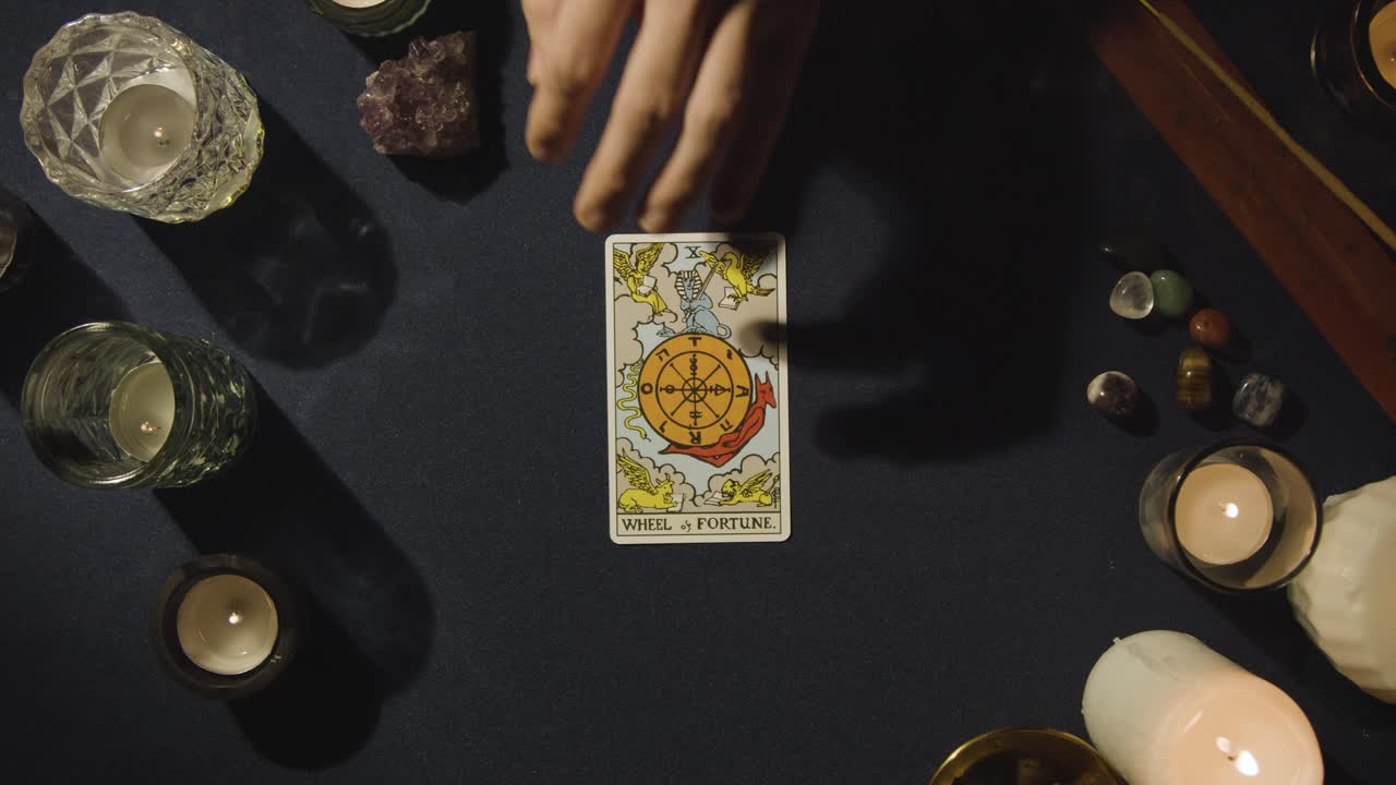 toma aérea de una persona que da una lectura de cartas del tarot colocando la rueda de la fortuna en la mesa