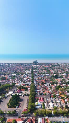 vertical drone shot of tuban regency in east java, indonesia, highlighting the cityscape with its blend of urban and natural landscapes and beach. the java sea is in the background.