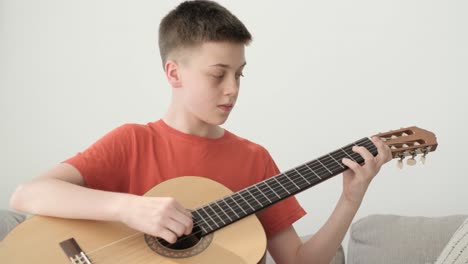 teenage boy playing guitar while sitting on sofa at home, play the musical instrument. the concept of learning to play a musical instrument. high quality fullhd footage