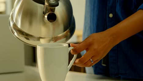 primer plano de una mujer negra vertiendo agua caliente en una taza de café en la mesa de comedor en la cocina 4k