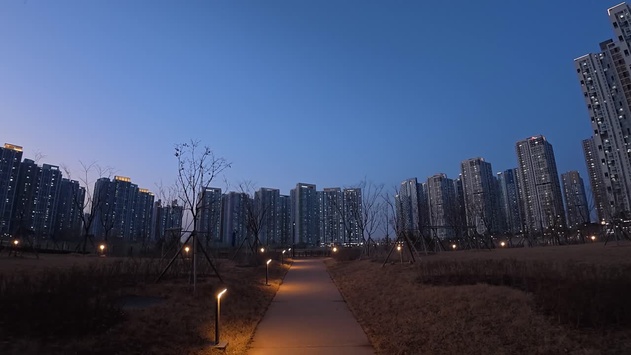 Park Pathway Illuminated At Dusk With Tall Apartment Buildings In Background. Incheon, South Korea. wide POV shot