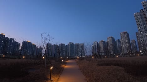 park pathway illuminated at dusk with tall apartment buildings in background. incheon, south korea. wide pov shot