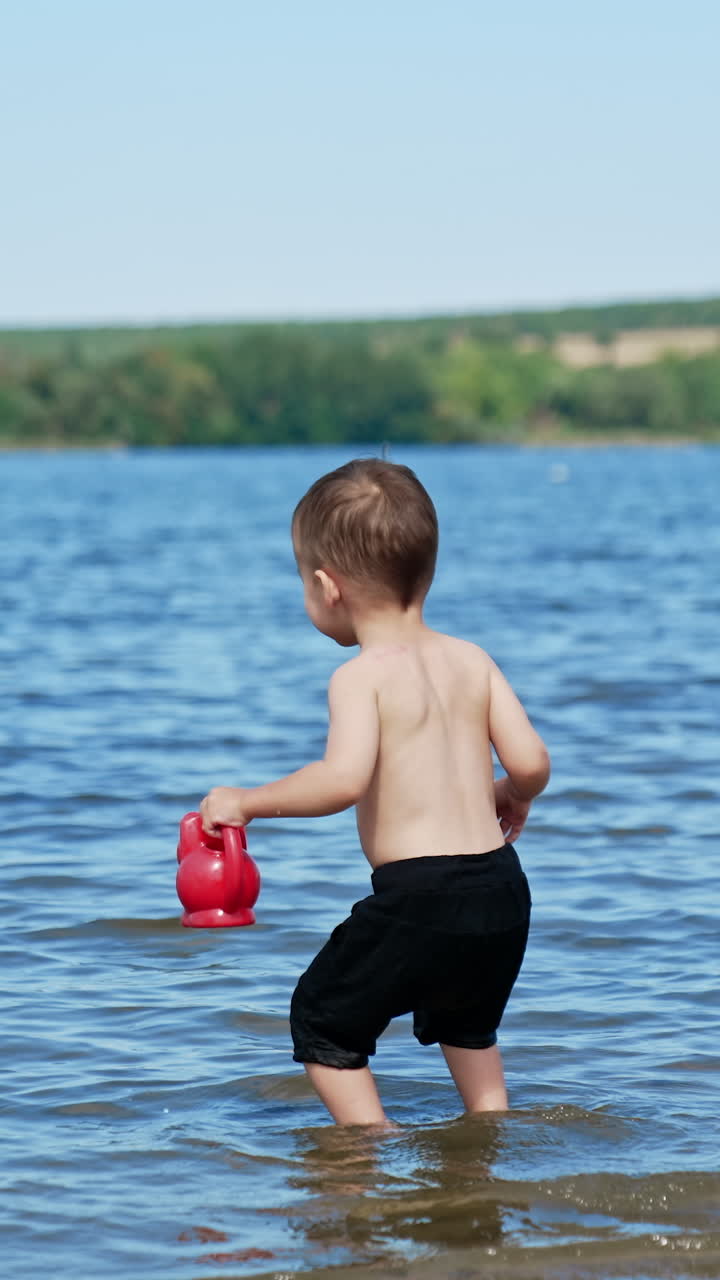 Summer sunny day and splashing on a beach. Small funny child playing on river with water. Vertical video
