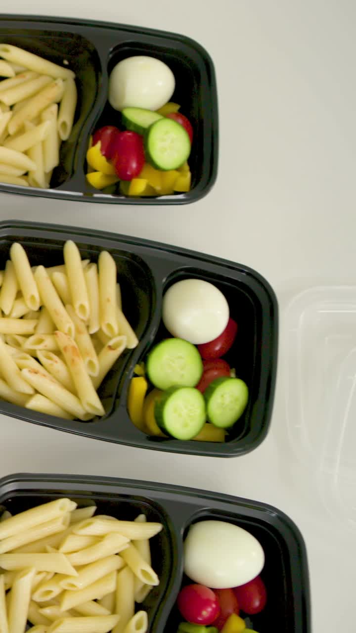 Vertical video: Reaching in, man in blue shirt arranging meal trays on counter for packing