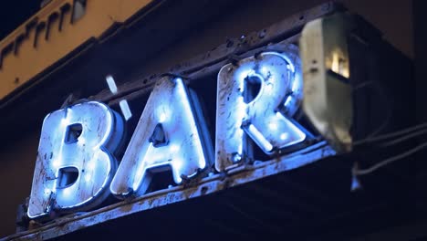 flickering vintage neon bar sign features some broken letters, creating a nostalgic atmosphere in a lively nightlife setting