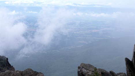 la toma de zoom estático desde el pico de la montaña rocosa ofrece una vista dramática de las tierras bajas brumosas de abajo.