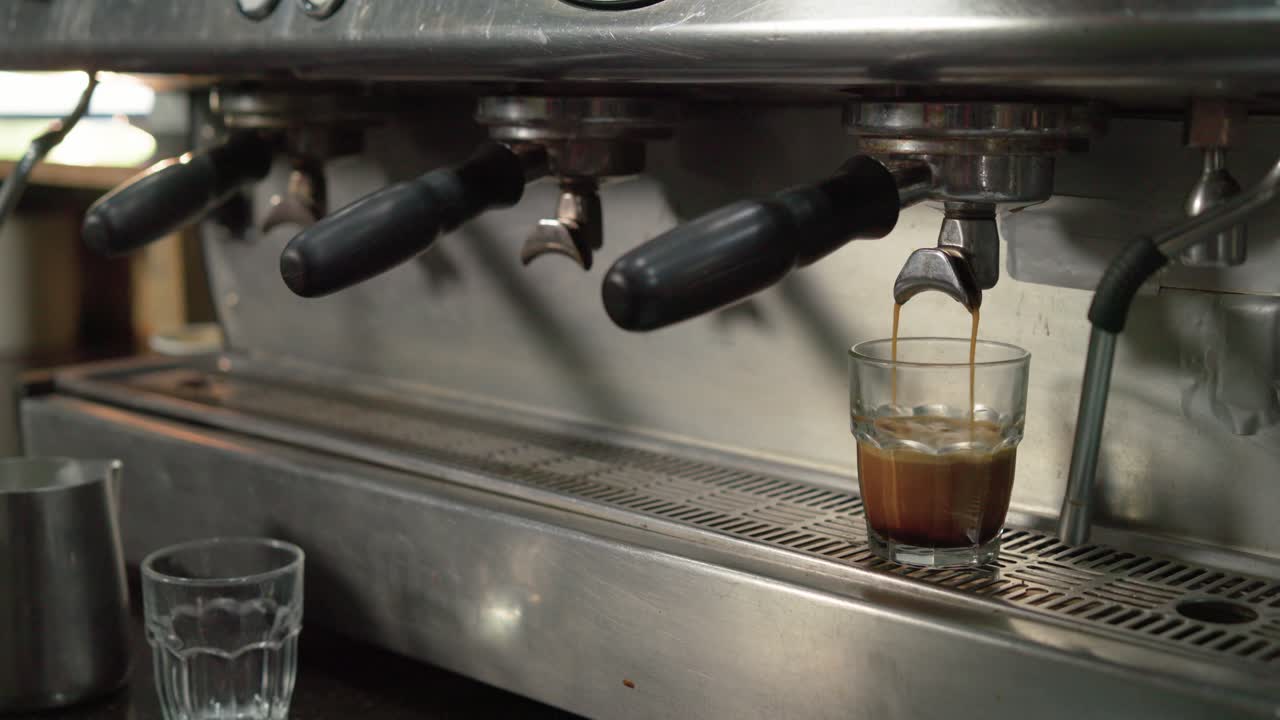 Il beccuccio della macchina sta iniziando a versare l'espresso nel bicchiere sul vassoio raccogligocce, estraendo la crema da servire