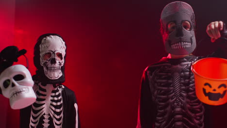 fotografía de estudio de niños vestidos con trajes de esqueleto haciendo trucos o tratamientos con cubos de caramelos en halloween con iluminación de fondo de humo rojo 1