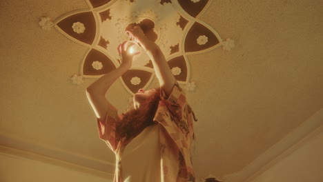 girl replacing lightbulb under ornate ceiling in sunlit room at home