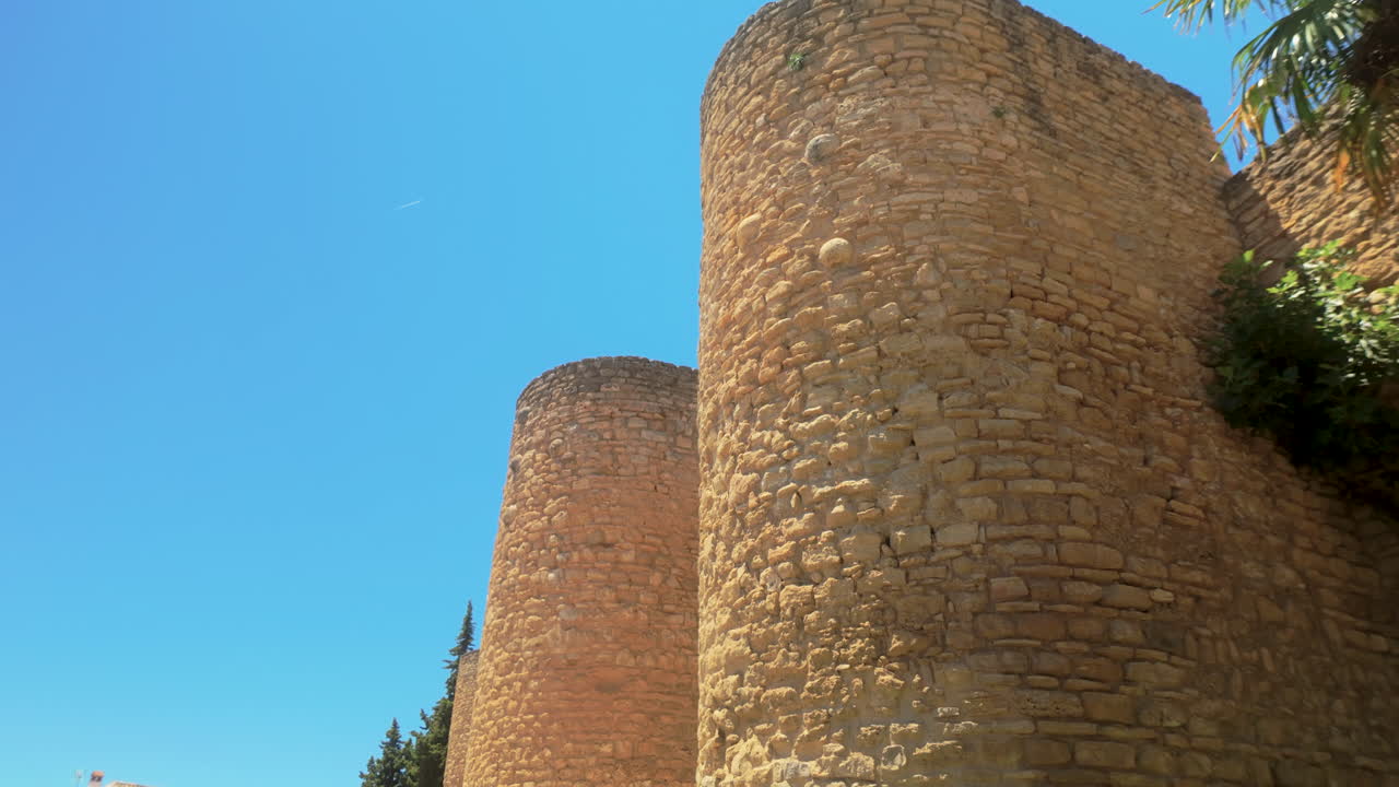 Fiori rosa in fiore davanti ad antiche torri di pietra, che catturano la fusione di storia e natura a Ronda, Spagna, sotto un cielo sereno