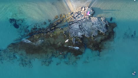 Drone-clip-moving-upwards-over-a-rock-formation-on-the-edge-of-a-tropical-beach-in-Calpe,-Spain