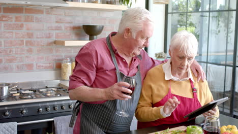 Pareja-Caucásica-Mayor-Cocinando-La-Cena-Usando-Una-Tableta-En-La-Cocina-De-Casa,-Cámara-Lenta