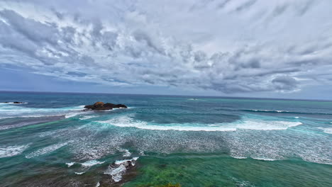 coastal view from sunset view hill in lombok, indonesia - turquoise waves splashing on rocky shore under dramatic sky. panning shot, slow motion