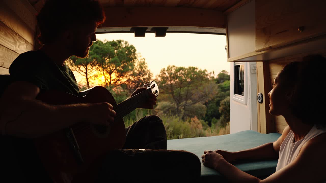 Couple enjoying music in a camper van at sunset