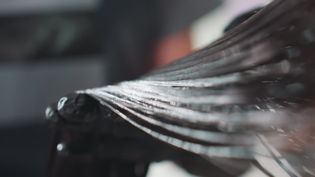 close examination of dye application technique, hands evenly distribute rich dark dye onto hair strands, detailed closeup of hands carefully applying intense black dye to each hair strand