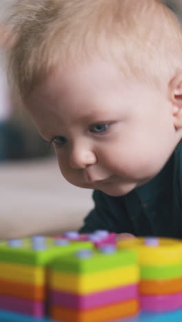 cute little boy plays with colorful plastic toy and blurred sister walks on background in bedroom close view