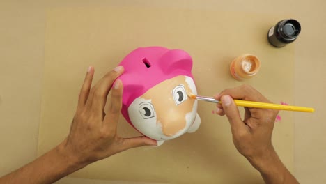 painting plaster piggy bank with paintbrush on brown paper at home