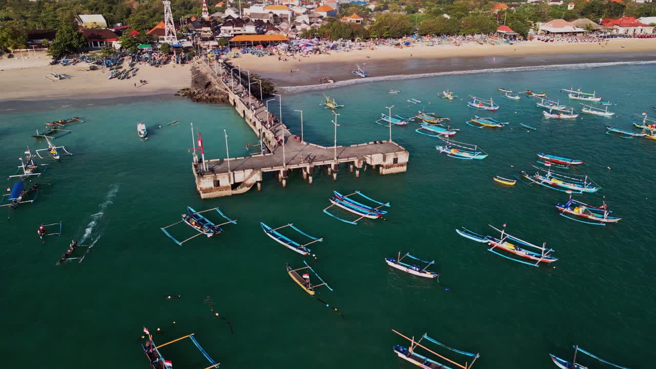 Traditional fishing boats in Bali line the turquoise waters around the pier, with sandy shoreline, vibrant coastal scenery, and island harbor life unfolding in a picturesque setting