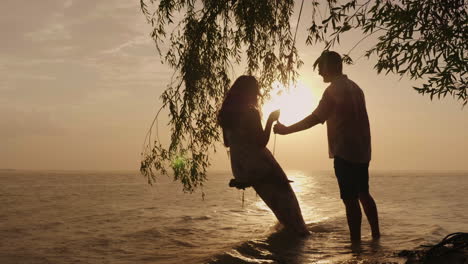 silhouettes of a young couple a man is rolling his wife on a swing against the background of the sea