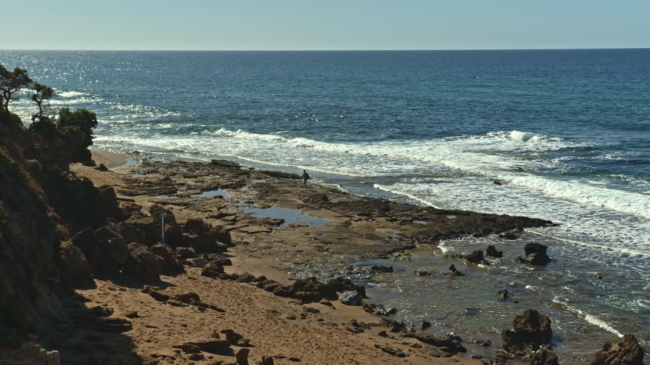 persona solitaria caminando en la costa rocosa con olas de mar en cerdeña, vista lejana