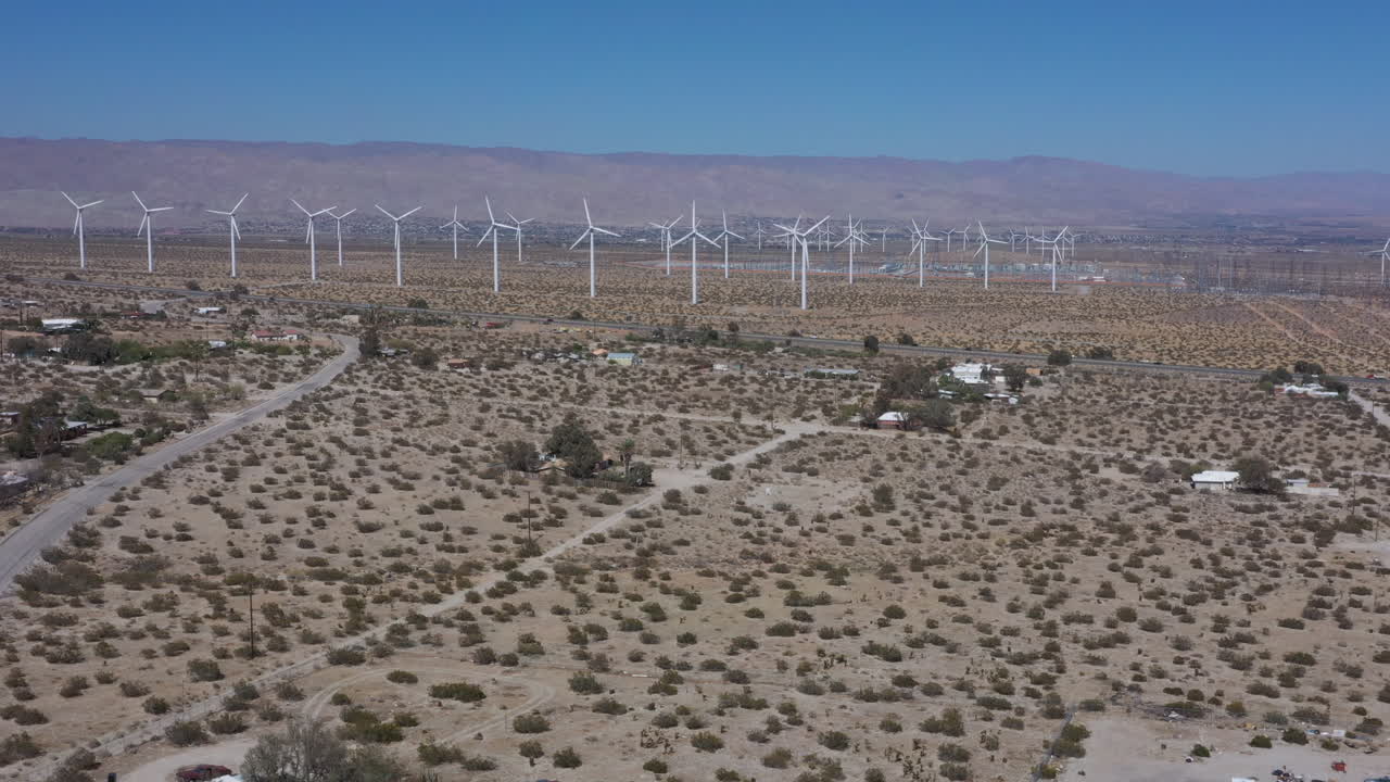 Renewable white turbine wind farm in western America countryside arid landscape with rotating onshore propellers generating green energy on bright blue sunny sky day, above aerial approach