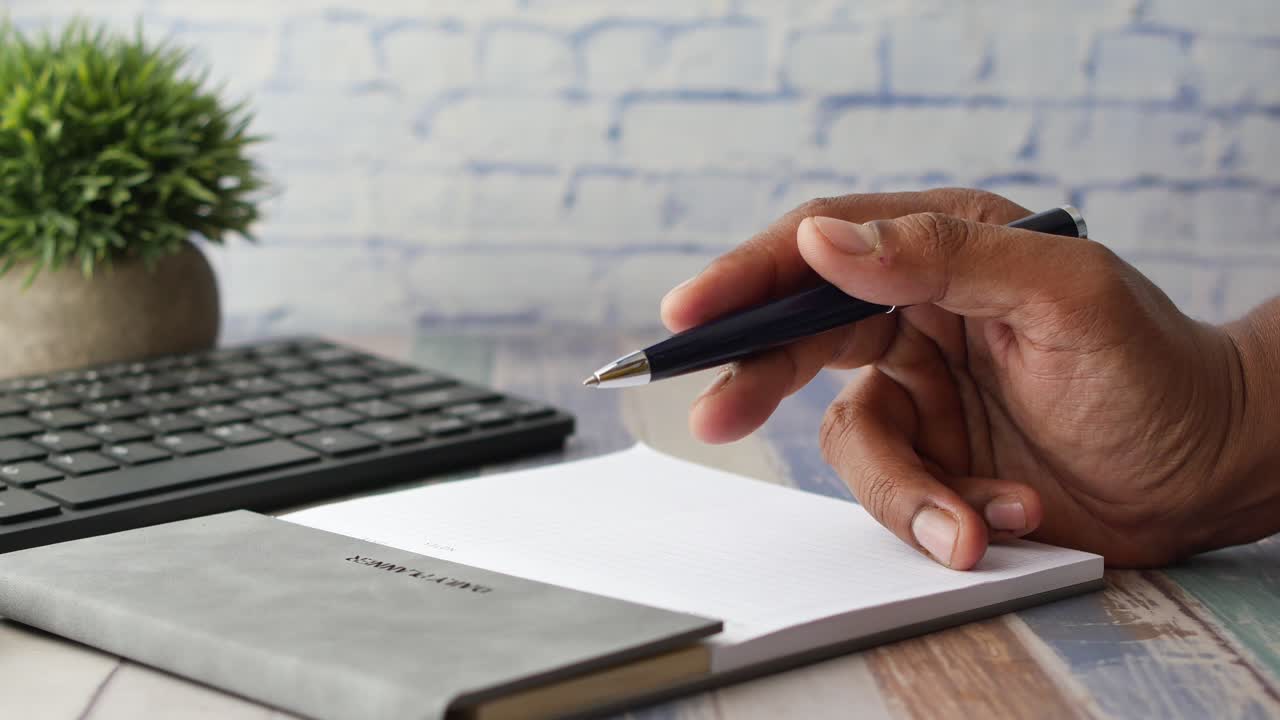 Mano de hombre escribiendo en un bloc de notas sentado